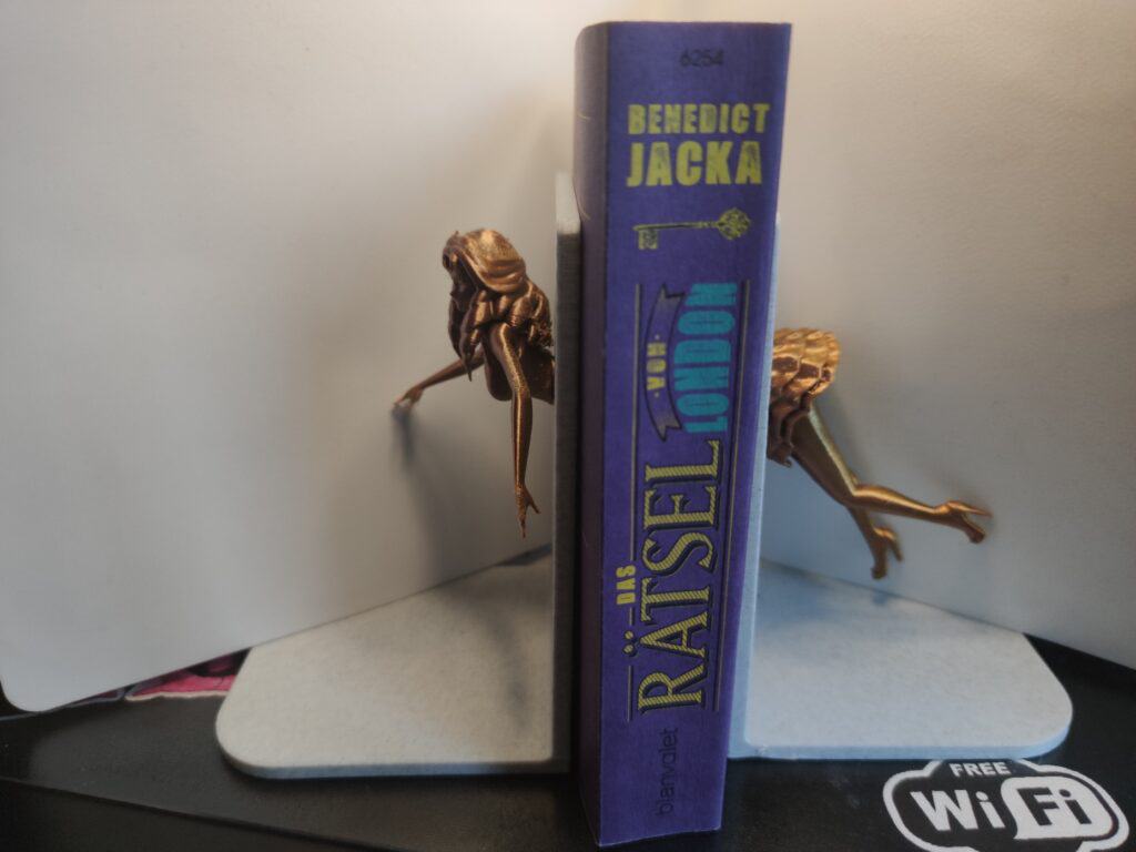 Buchstütze. Eine Frau tuacht durch die eine Buchstütze ein und sieht aus der anderen heraus. Dazwischen Bücher.