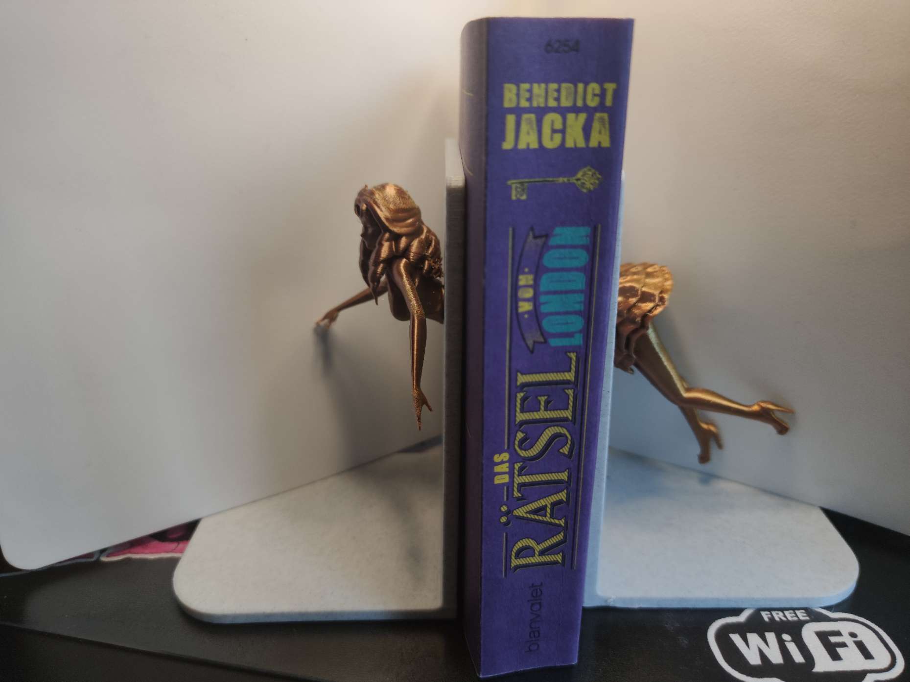 Buchstütze. Eine Frau tuacht durch die eine Buchstütze ein und sieht aus der anderen heraus. Dazwischen Bücher.